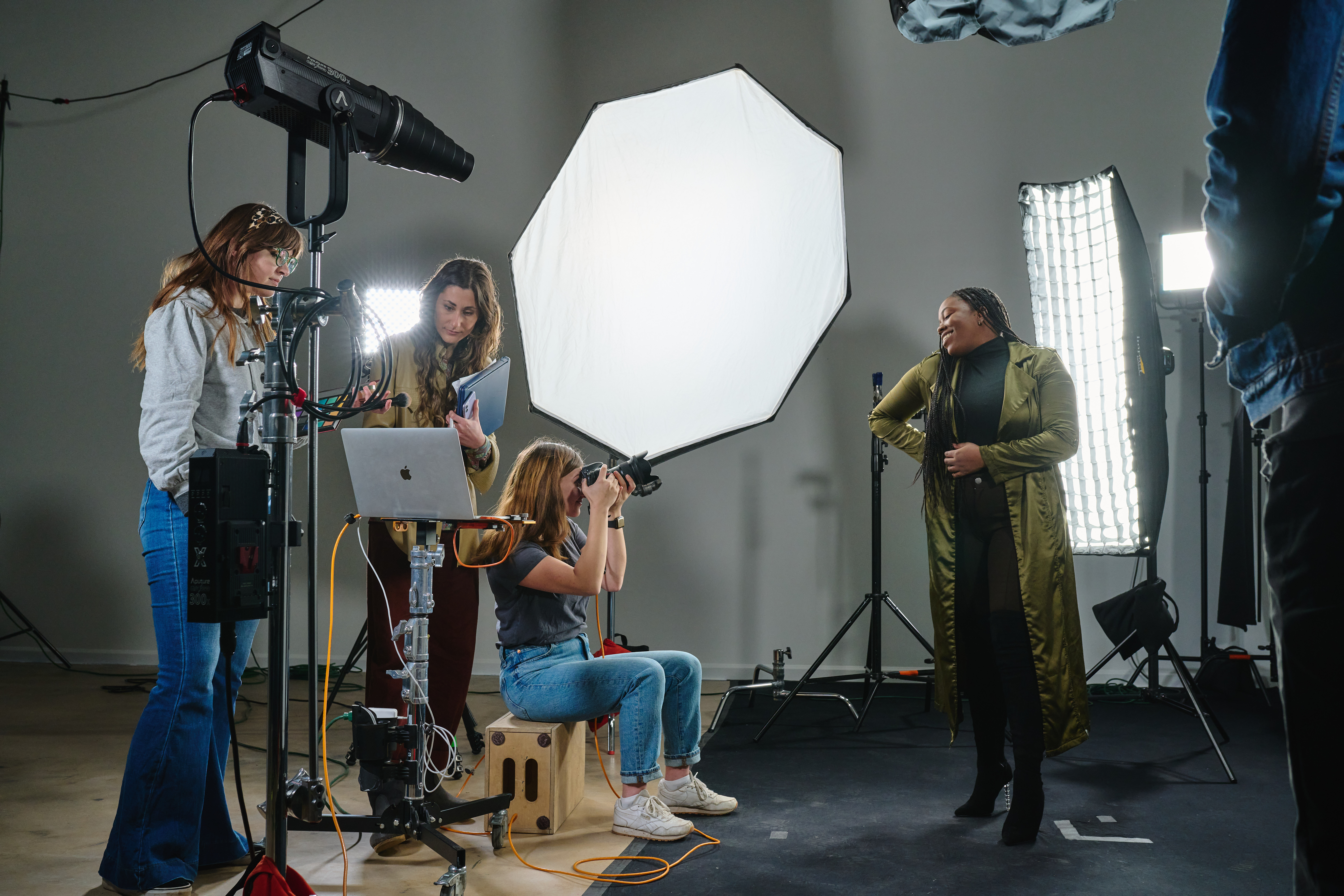 Photography studio setup with a model posing under studio lights, surrounded by a photographer and assistants adjusting equipment.